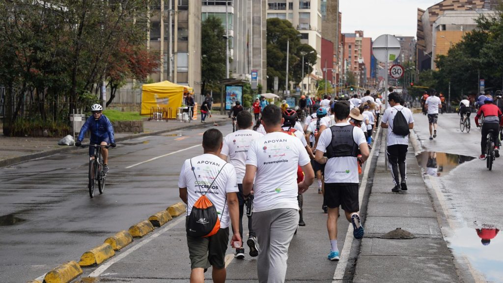 Varias personas se ven de espaldas,  trotando por la carrera séptima de Bogotá, con camisetas de "Corre por los Cerros" carrera que se llevó a cabo como evento previo a la COP16.